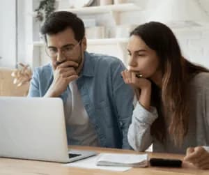 Two people sitting at a kitchen table reading a rental application on a laptop