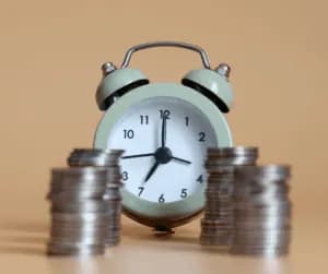 A small alarm clock standing between two stacks of coins